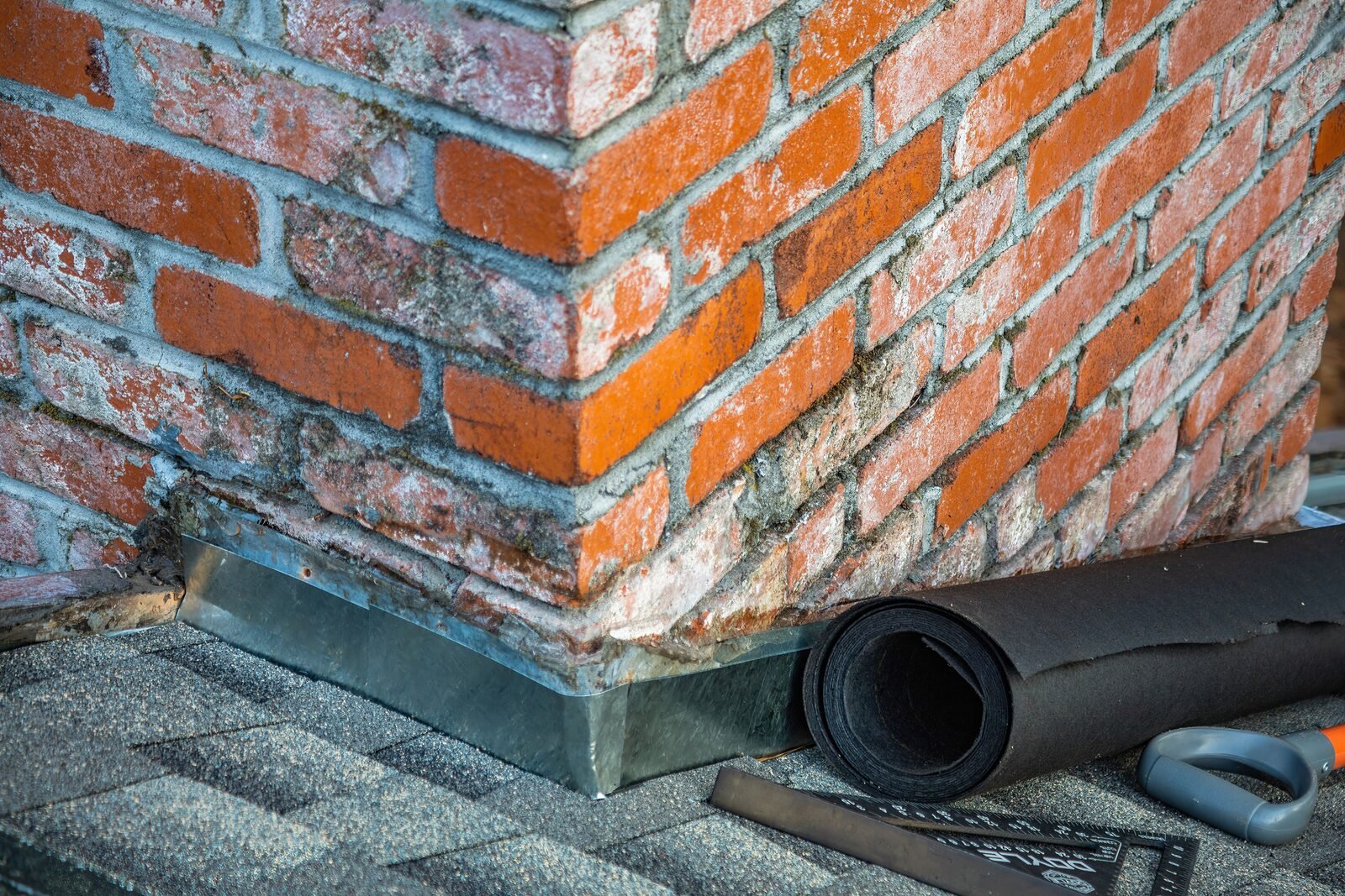 Close-up of chimney flashing repair with an underlayment roll visible on a Grand Rapids roof, the same class of material Michigan code requires as ice and water shield at the eaves