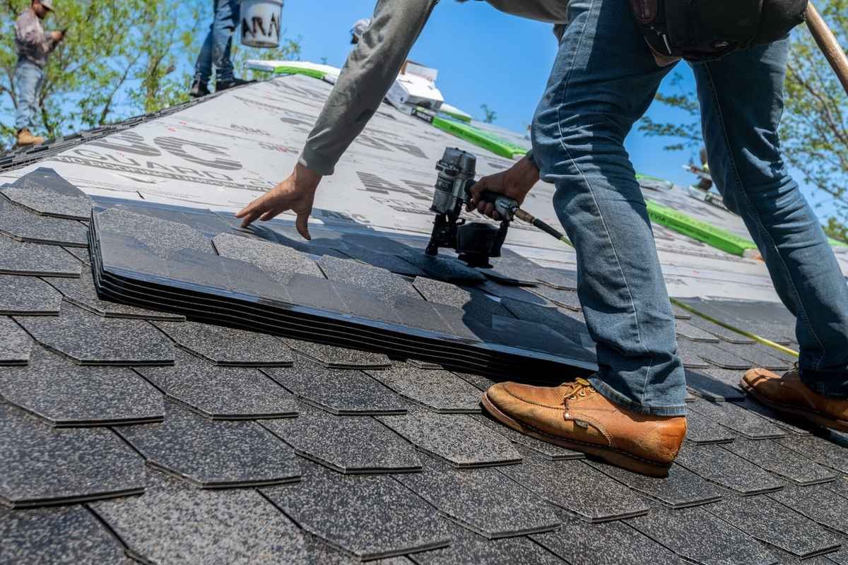 Roofer installing new asphalt shingles during a repair job in Grand Rapids, the kind of labor that factors into repair cost